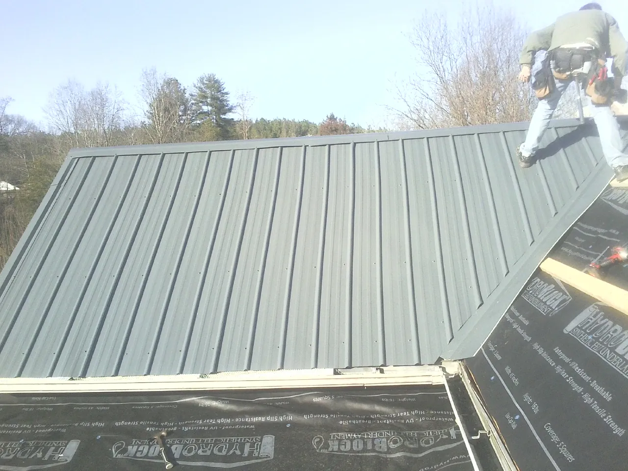Crew installing dark green standing seam panels over synthetic underlayment in Stratford